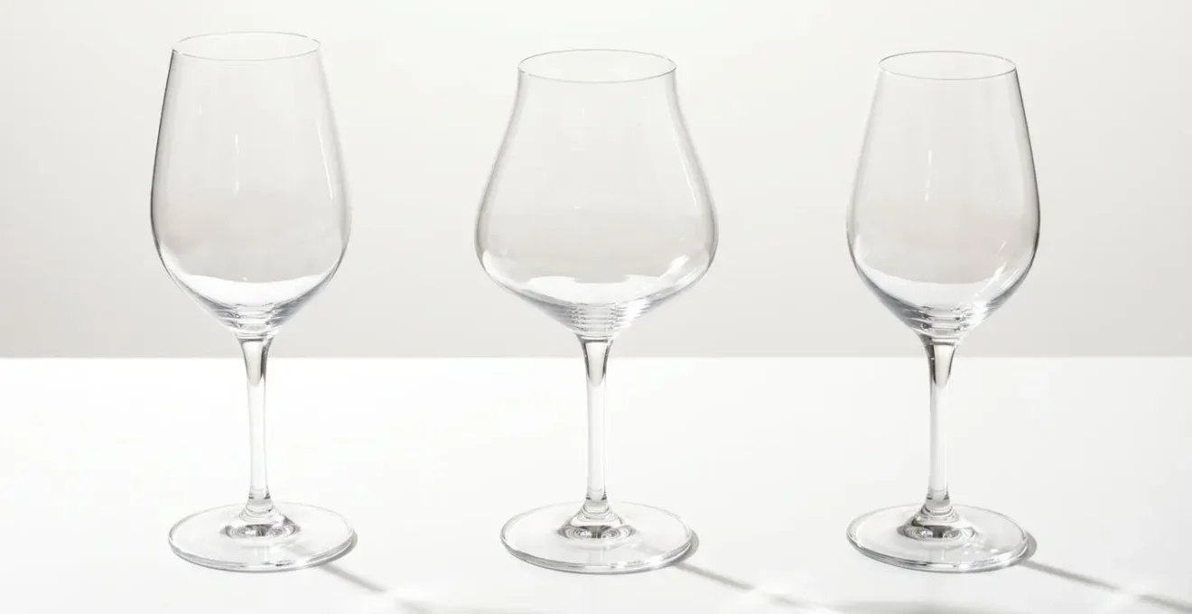 Trois verres à dégustation en cristallin de formes différentes alignés sur une surface blanche, lumière traversant le matériau révélant sa transparence